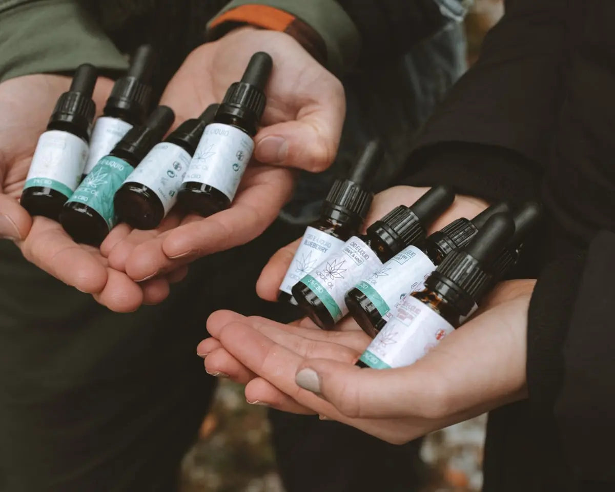 Zwei Personen halten viele Fläschchen CBD Liquid in den Händen