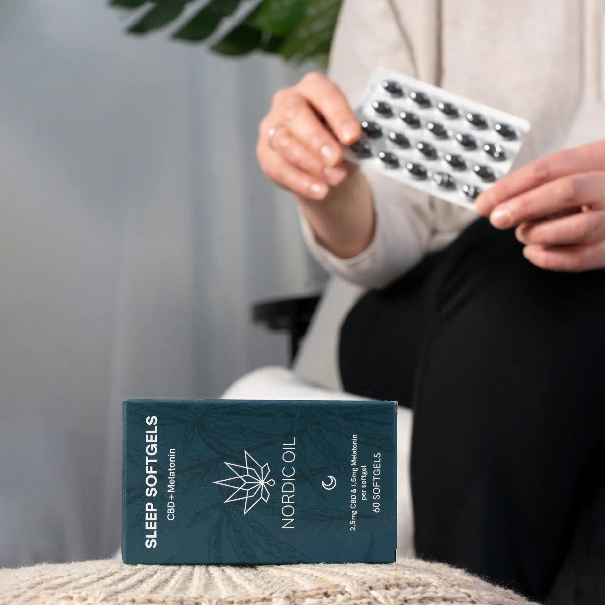 Frau im Hintergrund hält Softgels in der Schachtel und vorne liegt Nordic Oil CBD + Melatonin Softgels Packung