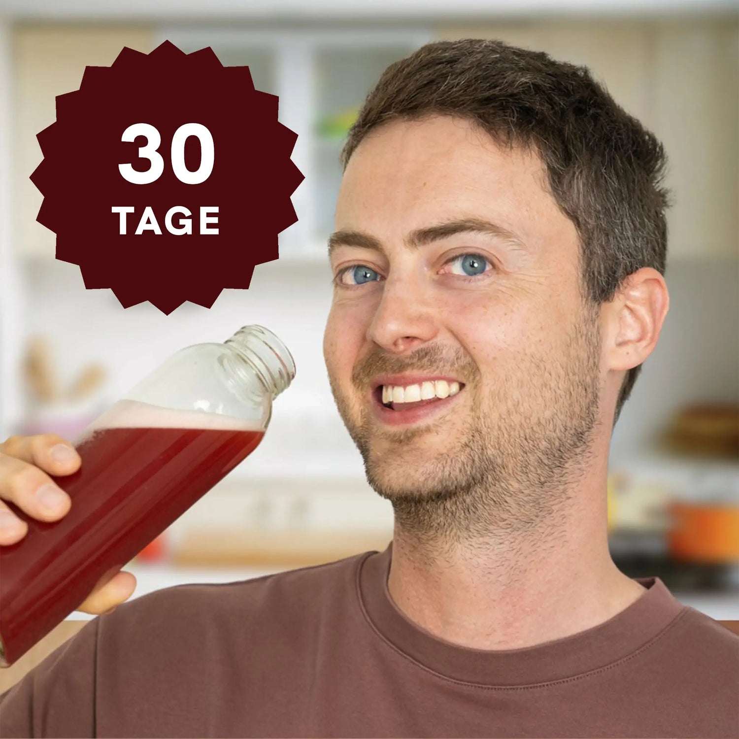 Mann in Küche hält Flasche mit rotem Getränk, 30 Tage-Aufkleber sichtbar.
