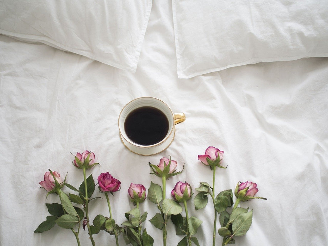 Auf einem Bett liegt eine Tasse Kaffe und Rosen