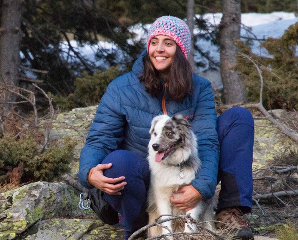 Eine Frau sitzt im Wald und hält ihren Hund.