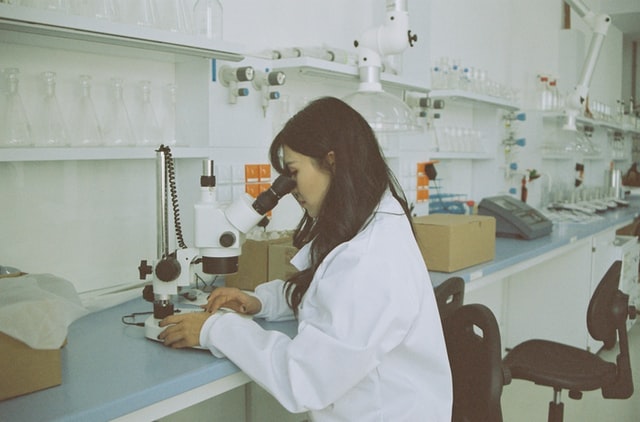 Eine Laborantin sitz in einem Labor an einem Mikroskop.