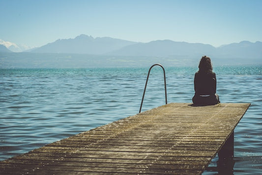 Eine Frau sitz am ende eines Stegs und schaut auf den See raus.