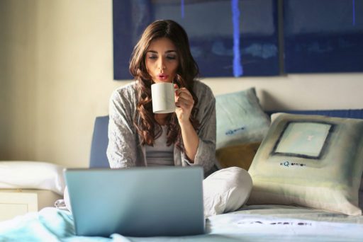 Frau mit Kaffee auf dem Bett am Laptop