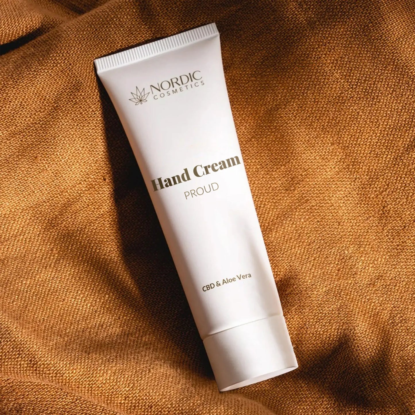 Handcreme-Tube von Nordic Cosmetics mit CBD & Aloe Vera auf braunem Stoff