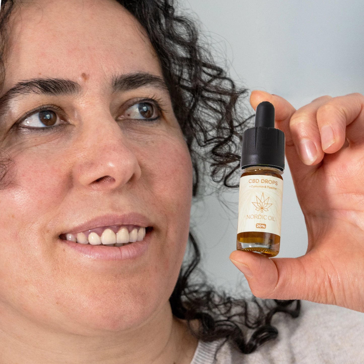 Eine Frau hält eine Flasche CBD Öl 20% Curcumin neben ihr Gesicht
