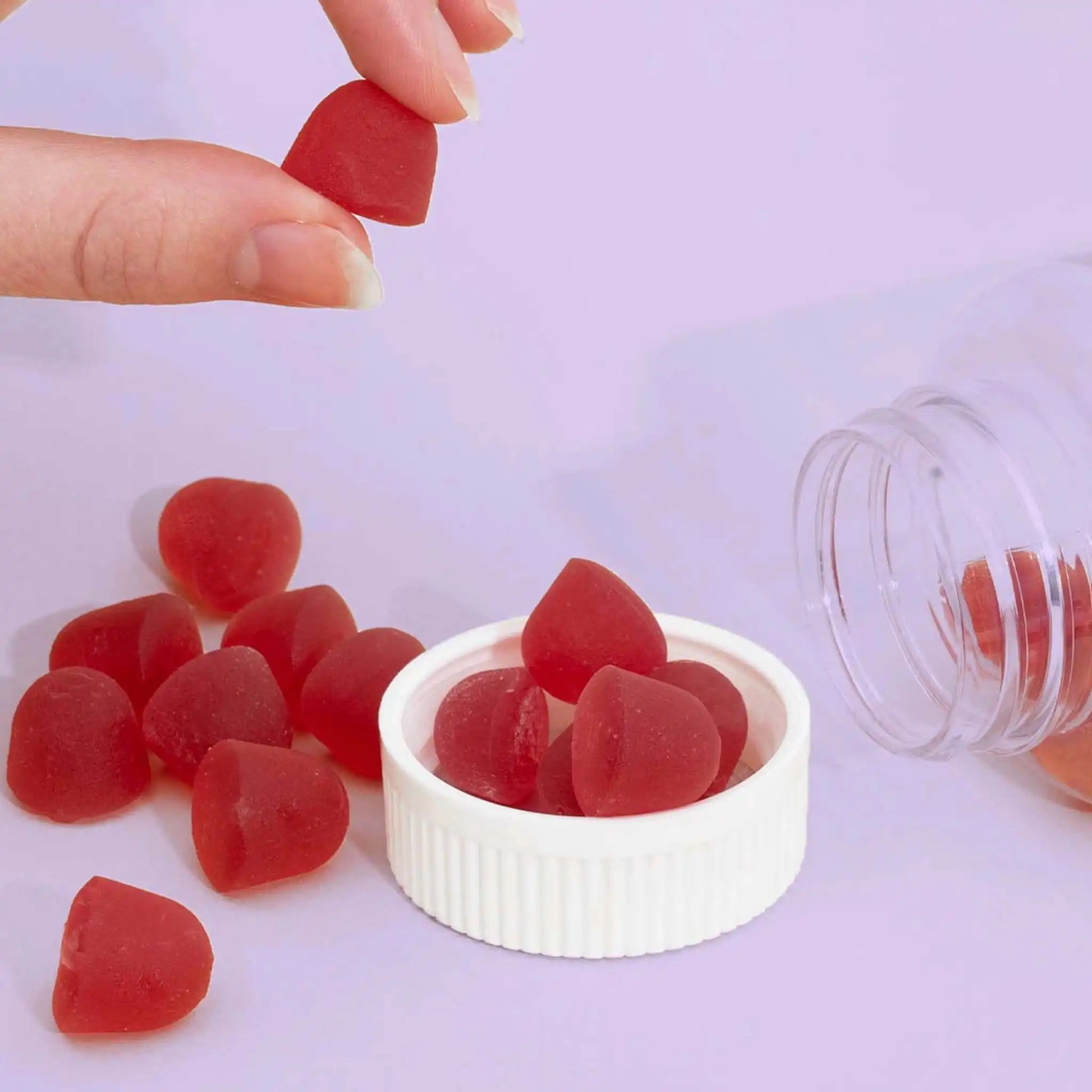 Kundin hält Fruchtgummi und mehre Fruchtgummis liegen auf Rosa Hintergrund