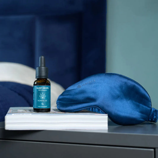Nordic Oil Sleep Drops stehen auf einem Nachttisch mit einem Buch und einer Schlafmaske 