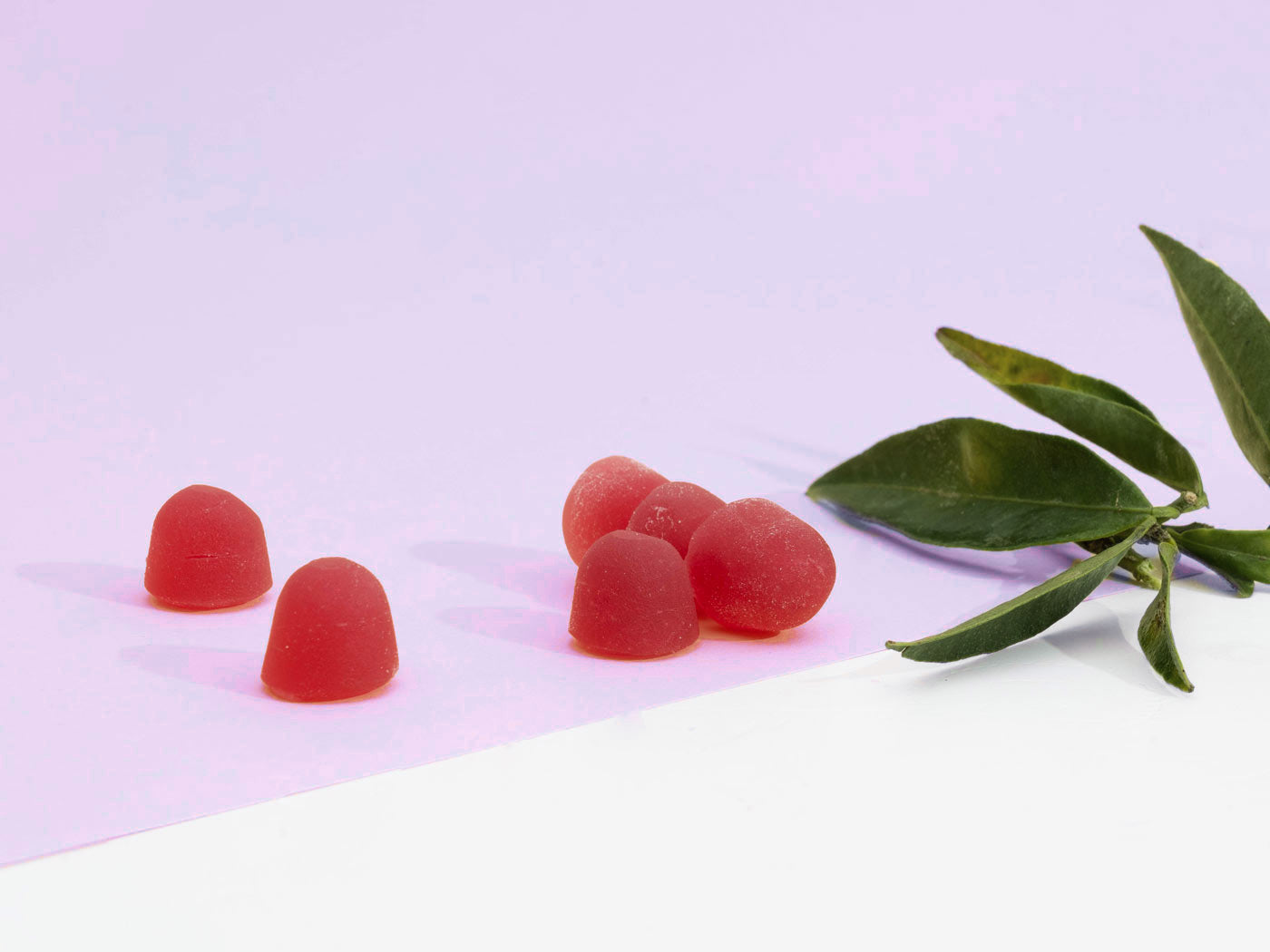 rote cbd gummies neben ein blatt mit pinken Hintergrund