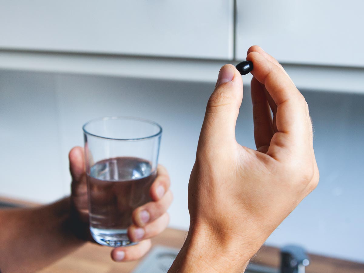 Eine Hand hält ein Glass Wasser und eine Kapsel.