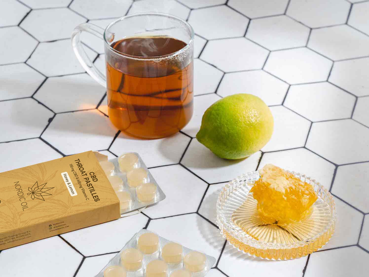 Eine Glas Tee steht neben einer Limone, Honig und dem CBD Halstabletten.