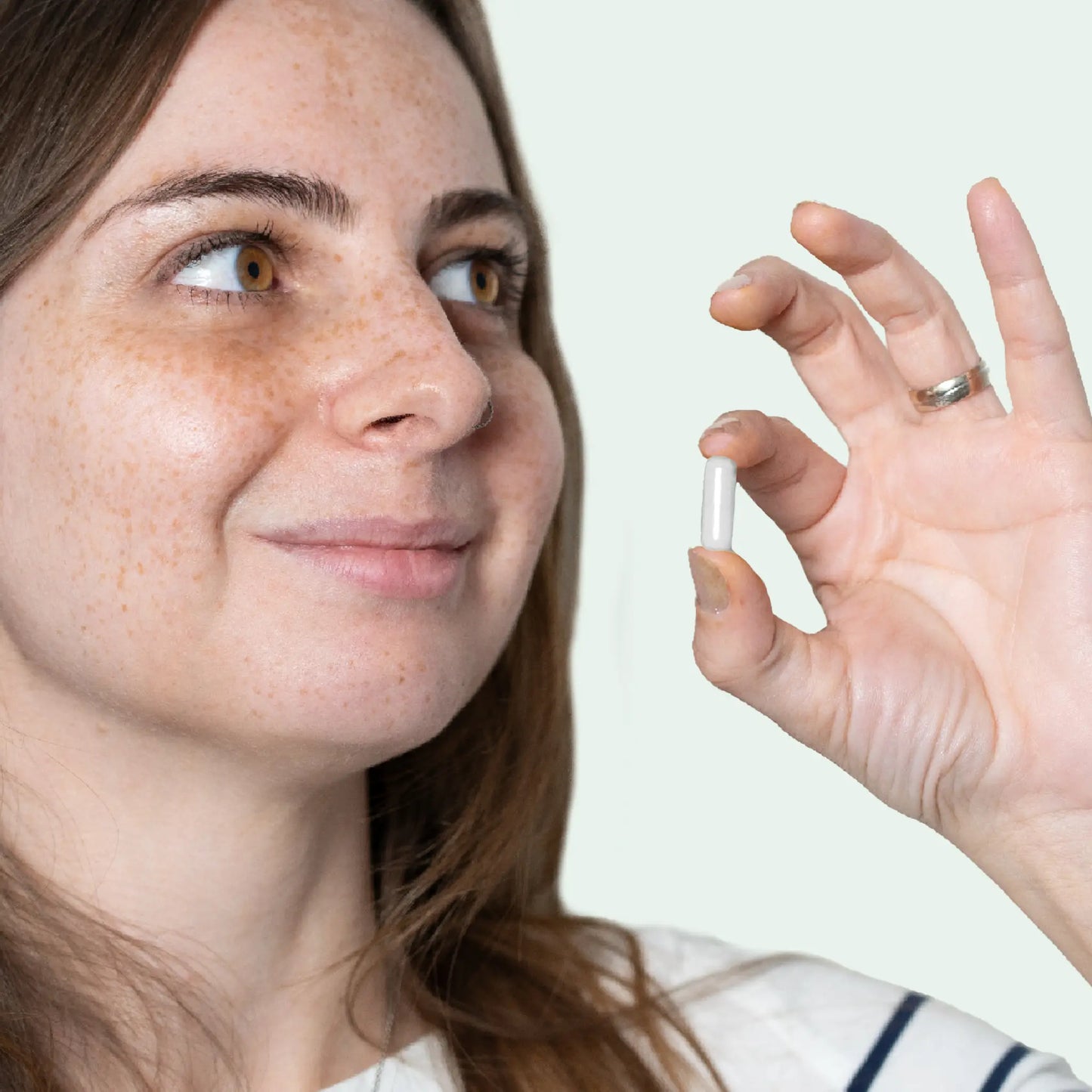 Nahaufnahme einer Frau, die eine weiße Kapsel zwischen Daumen und Zeigefinger hält